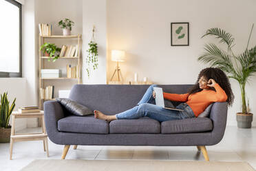 Young woman with laptop sitting on sofa in living room at home - JCZF01016