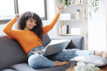 Smiling woman gesturing sitting with laptop on sofa at home - JCZF01028