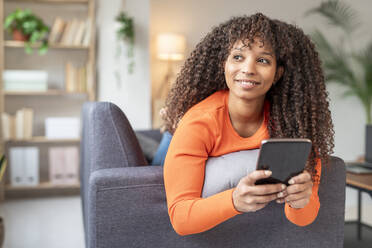 Lächelnde Frau mit Smartphone auf Sofa im Wohnzimmer zu Hause - JCZF01032