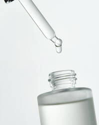 Natürliche Hyaluronsäure für die Hautpflege tropft aus einer Pipette in eine kleine Glasflasche auf weißem Hintergrund in einem hellen Raum - ADSF34536