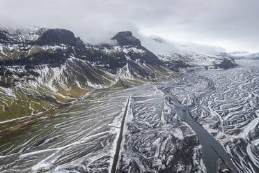 Luftaufnahme einer Flussmündung entlang der Bergkette im Winter in Island. - AAEF14409