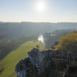 Luftaufnahme einer Frau, die bei Sonnenuntergang auf den Felsen mit der Burg Walzin im Hintergrund steht, Dinant, Namur, Belgien. - AAEF14440