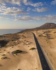 Luftaufnahme einer Straße entlang der Küste durch den Naturpark Sanddünen in Corralejo, Fuerteventura, Kanarische Inseln, Spanien. - AAEF14471