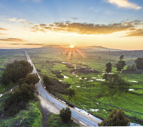Luftaufnahme einer Straße, die bei Sonnenaufgang über eine Wiese führt, Golanhöhen, Israel. - AAEF14509