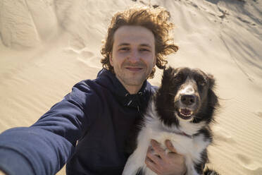Lächelnder junger Mann macht Selfie mit Hund an einem sonnigen Tag - SSGF00718