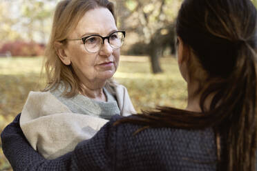 Senior woman wearing eyeglasses looking at healthcare worker in park - ABIF01638