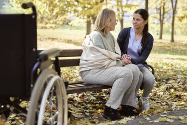 Ältere Frau im Gespräch mit einer Krankenschwester auf einer Bank im Park - ABIF01643