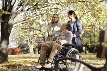 Lächelnder behinderter Mann mit Krankenschwester, der eine ältere Frau beim Gespräch im Park beobachtet - ABIF01649