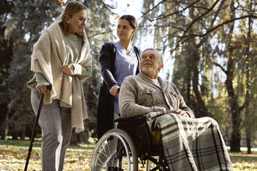 Senior man with nurse looking at woman walking with stick at park - ABIF01651