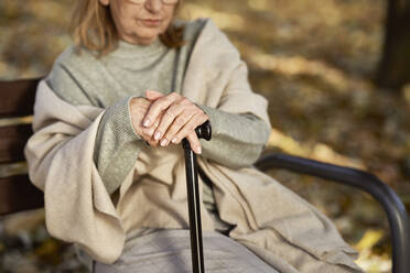 Senior woman with walking stick sitting on bench at park - ABIF01663