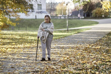 Ältere Frau geht mit Stock auf dem Fußweg im Park - ABIF01666