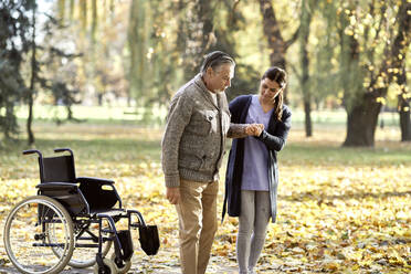 Gesundheitspflegerin hilft älterem behinderten Mann beim Gehen im Park - ABIF01668