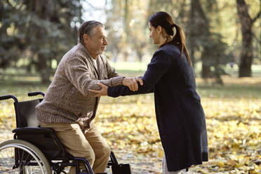 Krankenschwester hilft einem älteren behinderten Mann beim Aufstehen aus dem Rollstuhl im Park - ABIF01669