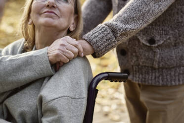 Behinderte Seniorin sitzt im Rollstuhl und tröstet Mann im Park - ABIF01671