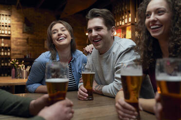 Eine Gruppe glücklicher Freunde trinkt Bier und unterhält sich in einer Kneipe - ABIF01676