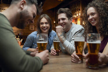 Eine Gruppe glücklicher Freunde trinkt Bier und unterhält sich in einer Kneipe - ABIF01678