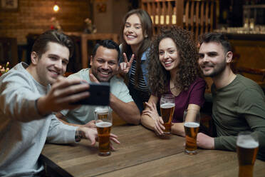 Eine Gruppe glücklicher Freunde trinkt Bier und macht ein Selfie in einer Kneipe - ABIF01681