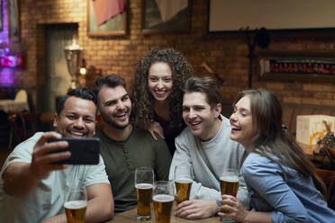Eine Gruppe glücklicher Freunde trinkt Bier und macht ein Selfie in einer Kneipe - ABIF01682