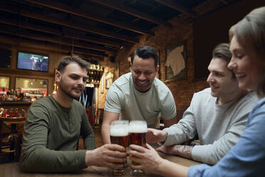 Freunde treffen sich in einer Kneipe und stoßen mit Biergläsern an - ABIF01687