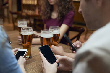 Freunde trinken Bier und benutzen Smartphones in einer Kneipe - ABIF01689