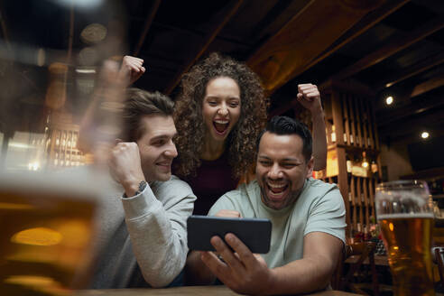 Fröhliche Fußballfans trinken Bier und schauen sich ein Spiel auf dem Smartphone in einer Kneipe an - ABIF01694