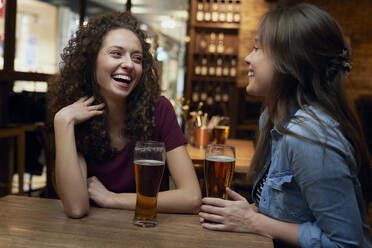 Two happy female friends having beer and socializing in a pub - ABIF01703