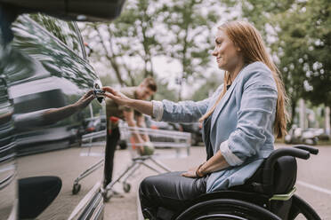 Lächelnde junge Frau, die im Rollstuhl sitzt und die Autotür öffnet - MFF08998