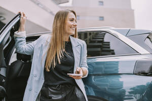 Glückliche Frau mit Mobiltelefon an der Autotür stehend - MFF08999