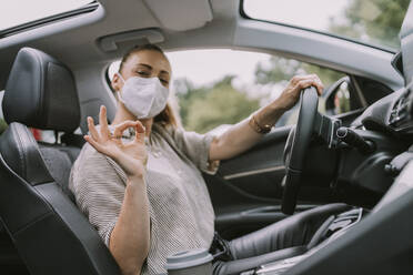 Frau mit Schutzmaske und OK-Geste im Auto - MFF09005