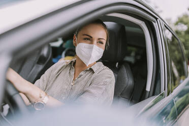 Woman wearing protective face mask sitting in car - MFF09007