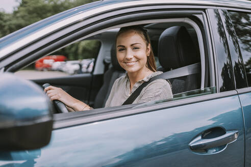 Lächelnde junge Frau schaut durch ein Autofenster - MFF09012