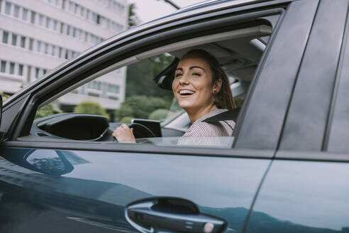 Glückliche junge Frau schaut durch das Autofenster auf die Straße - MFF09013