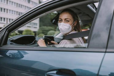 Junge Frau mit Gesichtsschutzmaske schaut durch ein Autofenster - MFF09014