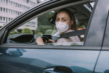 Young woman wearing protective face mask looking through car window - MFF09014