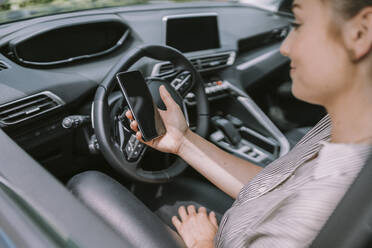 Woman with smart phone sitting on driver's seat in car - MFF09015