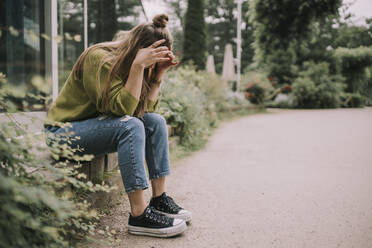 Stressed woman with head in hands sitting on wall at park - MFF09021