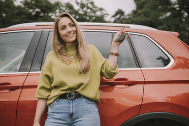 Lächelnde junge Frau mit Schlüssel vor einem Auto stehend - MFF09025