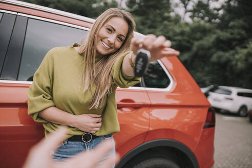Happy young woman handing over car key to friend on parking lot - MFF09026