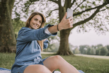 Lächelnde Frau nimmt Selfie durch Smartphone im Park - MFF09060