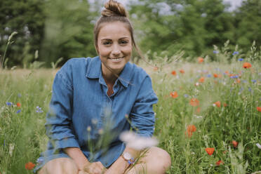 Smiling young woman sitting in meadow - MFF09067