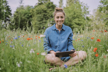 Smiling young woman with tablet PC sitting in meadow - MFF09074