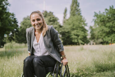 Happy woman sitting in wheelchair at park - MFF09077