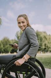 Lächelnde Frau mit Mobiltelefon im Rollstuhl im Park - MFF09081