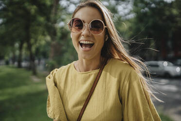 Glückliche blonde Frau mit Sonnenbrille im Park - MFF09085