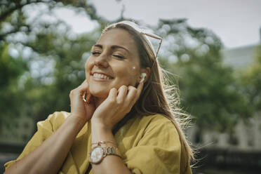 Lächelnde Frau hört Musik über Bluetooth im Park - MFF09086