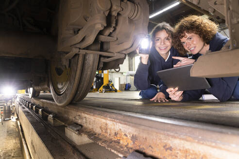 Ingenieur mit Tablet-PC bei der Analyse eines Einschienenrads mit einem Auszubildenden in einer Fabrik - FKF04779