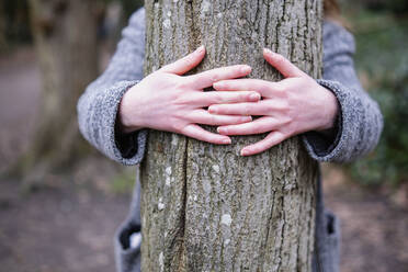 Junge Frau umarmt Baumstamm im Wald - AMWF00221