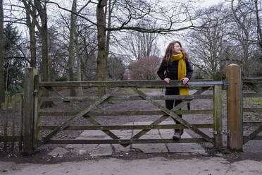 Happy woman standing on gate in forest - AMWF00230