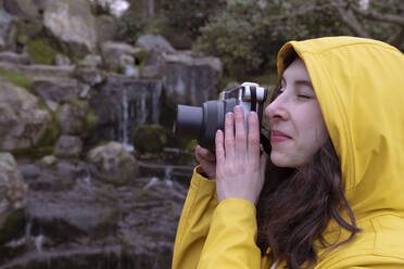Junge Frau schaut durch die Kamera beim Fotografieren im Wald - AMWF00236