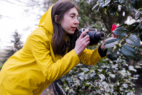 Junge Frau fotografiert Blume durch Kamera im Wald - AMWF00237